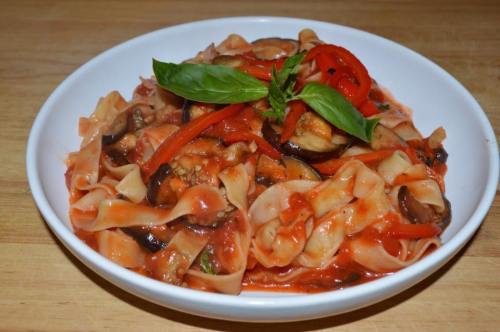 A bowl of pasta with eggplant, red peppers, and basil in a rich tomato sauce.