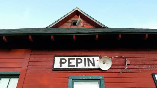 A close-up of a red building with a sign reading "PEPIN" and a light fixture on the side.