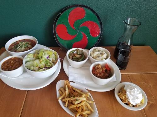 A colorful spread of salads, beans, fries, and a dessert, with a decorative plate and drinks on a wooden table.