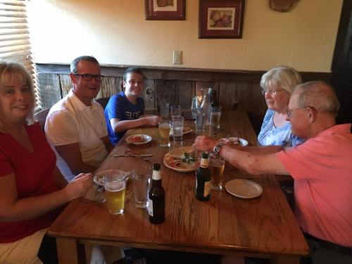 A group of five people enjoying a meal at a wooden table with drinks and plates of food.