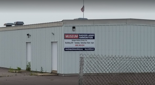 Exterior of the Badger Army Ammunition Museum building, featuring a sign with operating hours and contact information.