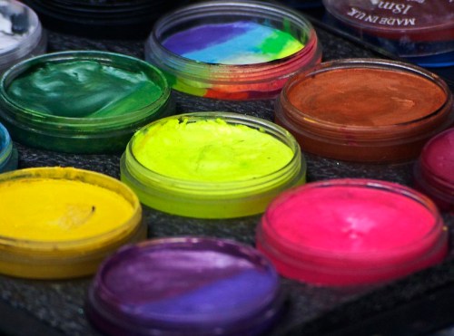 A close-up of colorful paint pots in various shades, including green, yellow, pink, and purple, arranged in a tray.