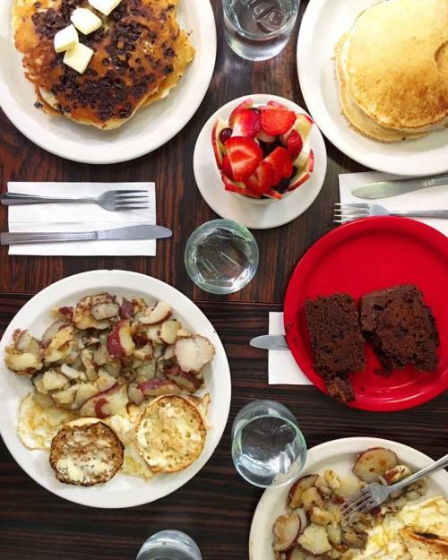 A table spread with pancakes, potatoes, eggs, chocolate cake, and a bowl of strawberries, accompanied by glasses of water.