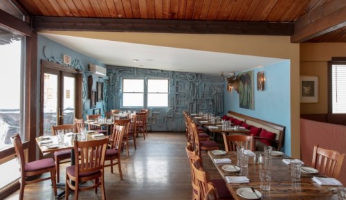 Interior of a cozy restaurant featuring wooden tables, chairs, and a blue wall with unique decor.