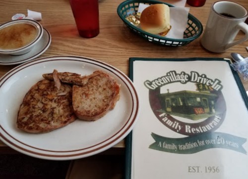 A plate with grilled meat and toast, alongside a menu and a cup of coffee at Green Village Drive-In restaurant.