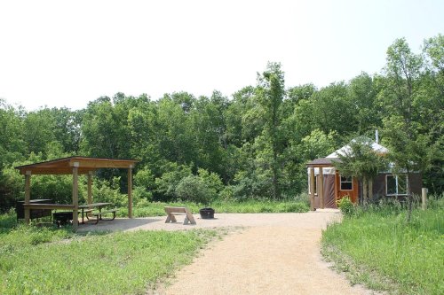 A path leads to a yurt and a picnic area with a shelter, surrounded by lush greenery and trees.