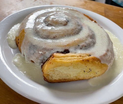 A large cinnamon roll topped with creamy icing, sitting on a white plate.