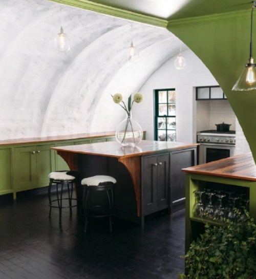 A modern kitchen with green cabinets, a wooden countertop, and a cozy dining area featuring a vase of flowers.