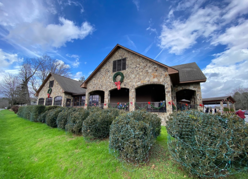 A stone building decorated for the holidays, surrounded by green bushes and a blue sky with scattered clouds.