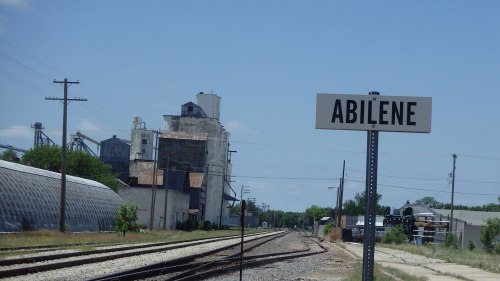 Sign for Abilene next to railway tracks, with industrial buildings and a clear blue sky in the background.