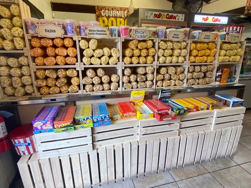 A colorful display of gourmet popcorn flavors and candy boxes in a shop, with wooden crates and a sign overhead.