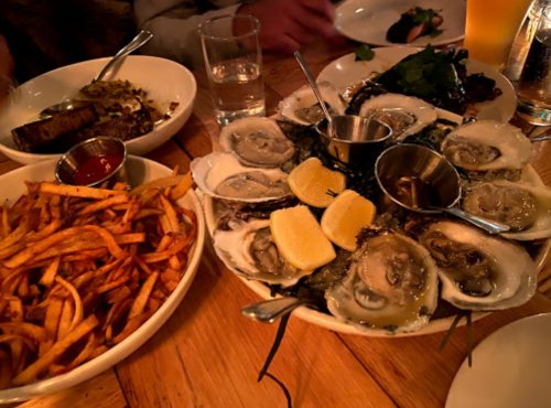 A table spread featuring a platter of oysters with lemon, alongside fries and other dishes in a dimly lit setting.