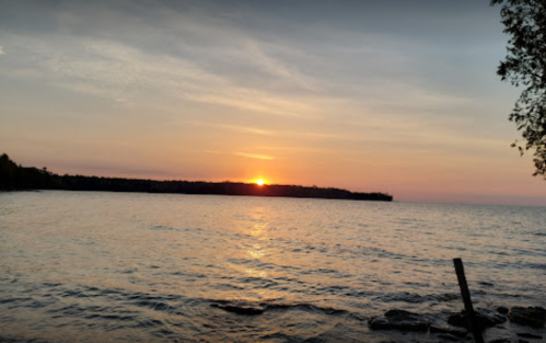 Sunset over a calm lake, with gentle waves and a silhouette of trees along the shoreline.