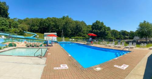 A sunny outdoor pool area with a slide, lounge chairs, and umbrellas surrounded by trees.