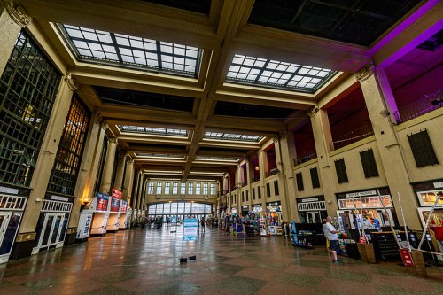 Interior of a spacious, historic train station with high ceilings, large windows, and bustling activity.