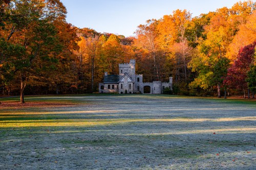 A stone castle surrounded by vibrant autumn trees and a frosty lawn under a clear blue sky.