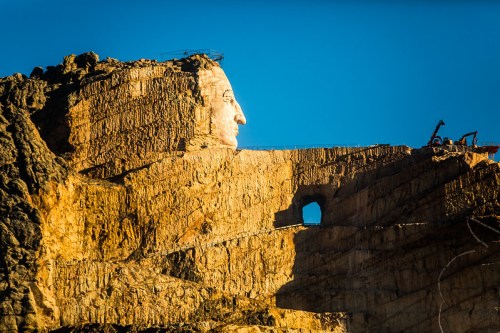 A large stone sculpture of a face carved into a rocky cliff, with a clear blue sky in the background.