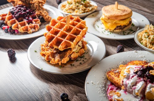 A variety of delicious dishes featuring waffles, fried chicken, and sides, beautifully arranged on white plates.