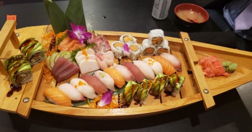 A wooden boat filled with various sushi rolls, sashimi, and garnishes like wasabi and pickled ginger.