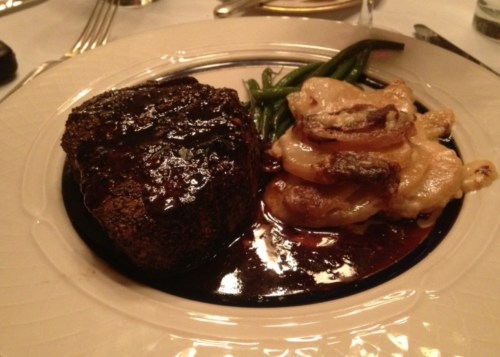 A plated meal featuring a grilled steak, creamy potatoes, and green beans, garnished with a rich sauce.