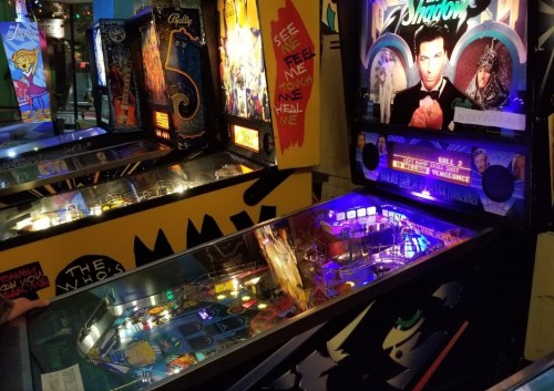 A vibrant arcade scene featuring two pinball machines with colorful lights and themed artwork.