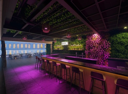 A stylish rooftop bar with vibrant greenery, pink lighting, and a sleek counter, overlooking a cityscape.