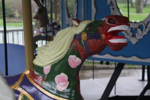 A colorful carousel horse with a vibrant mane and floral designs, set against a blurred background of a carousel.