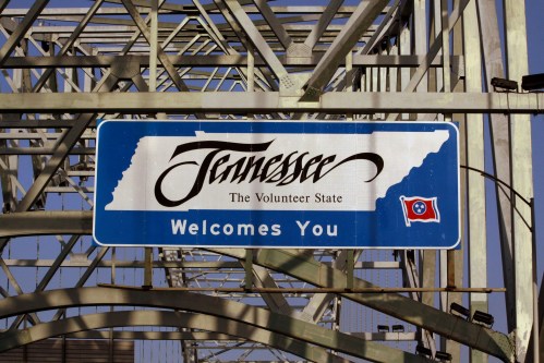 Sign welcoming visitors to Tennessee, featuring the state outline and flag, with the text "Tennessee The Volunteer State Welcomes You."