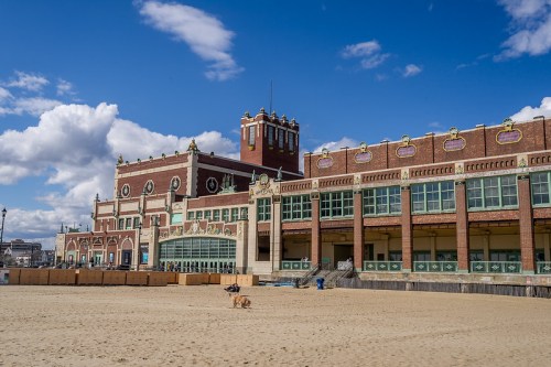 Historic beachfront building with a sandy area in front, under a blue sky with scattered clouds.
