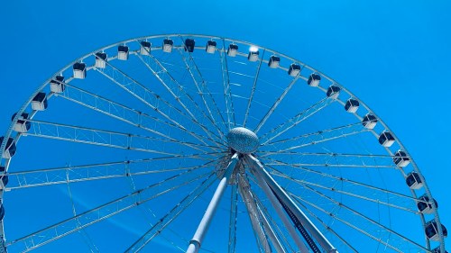A large Ferris wheel against a clear blue sky, showcasing its structure and passenger cabins.