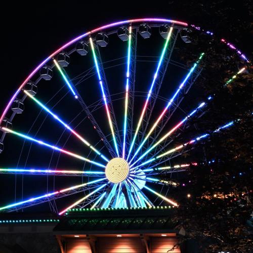 A brightly lit Ferris wheel at night, featuring vibrant, colorful lights against a dark sky.