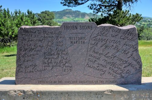 A stone historic marker with inscriptions about pioneers and their experiences, set against a green landscape.