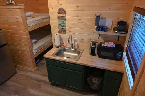 Cozy cabin interior featuring a kitchenette, bunk beds, and wooden walls.