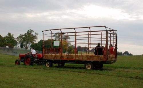 A red tractor pulls a hayride trailer with people sitting inside, set against a cloudy sky and green fields.