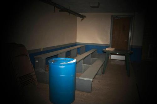 Dimly lit room with blue walls, featuring benches, a table, a blue barrel, and a closed door.