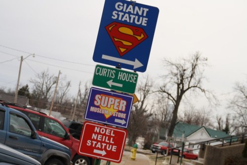 Signpost featuring directions to a giant Superman statue, Curtis House, and the Super Museum & Store, with Noel Neill Statue.