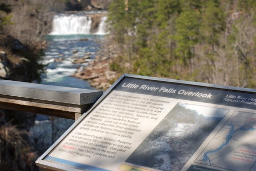 Sign at Little River Falls Overlook with a view of the waterfall and surrounding trees in the background.