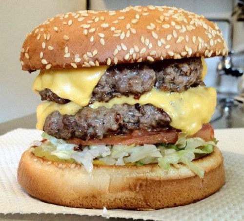 A large cheeseburger with two beef patties, melted cheese, lettuce, and tomato on a sesame seed bun.