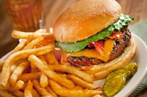 A juicy cheeseburger with lettuce, bacon, and a side of crispy fries and pickles on a plate.
