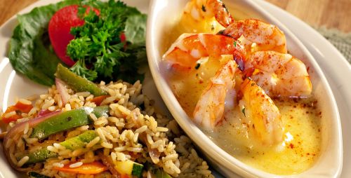 A plate of shrimp in a creamy sauce, served with rice and a side of salad with tomato and parsley.
