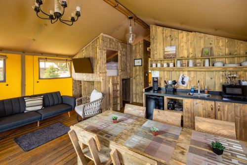 Cozy interior of a wooden cabin with a living area, kitchen, and dining table, featuring warm colors and natural light.