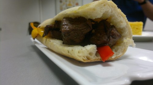 A close-up of a sandwich filled with grilled beef and colorful bell peppers, served on a white plate.
