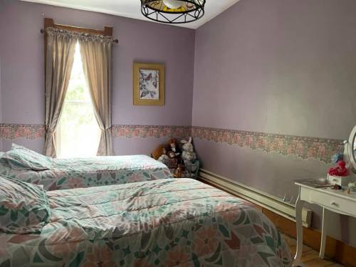 A cozy bedroom with two beds, floral bedding, a window with curtains, and a small vanity with decorative items.