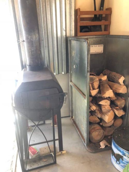 A wood stove next to a metal storage unit filled with stacked firewood in a garage or shed.