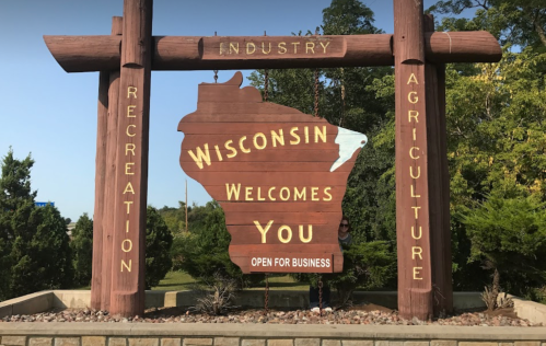 A large wooden sign welcoming visitors to Wisconsin, highlighting industry, recreation, and agriculture.