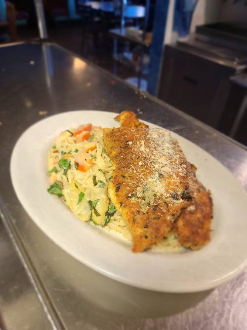 A plate of fried fish served over creamy pasta with vegetables, garnished with grated cheese.