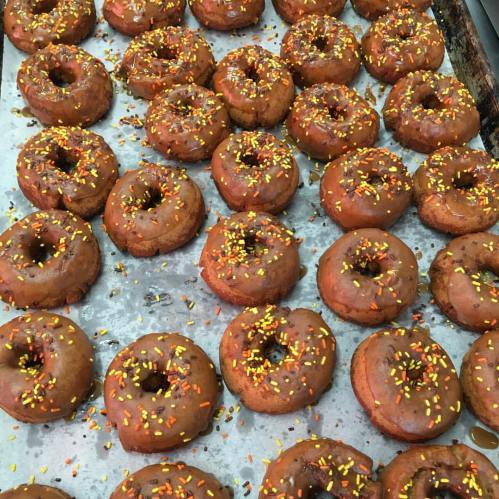 A tray of freshly baked donuts topped with orange and yellow sprinkles.