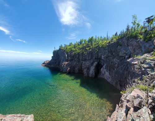 A serene coastal scene featuring rocky cliffs and clear blue water under a bright sky with scattered clouds.