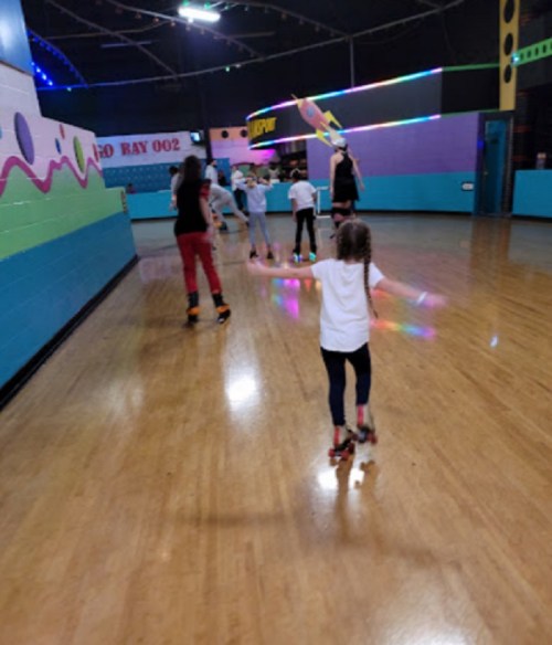 A group of children roller skating in a colorful indoor rink with lights and a smooth wooden floor.