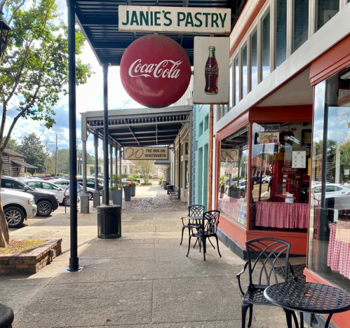 A storefront with "Janie's Pastry" sign and a Coca-Cola sign, featuring outdoor seating and parked cars nearby.